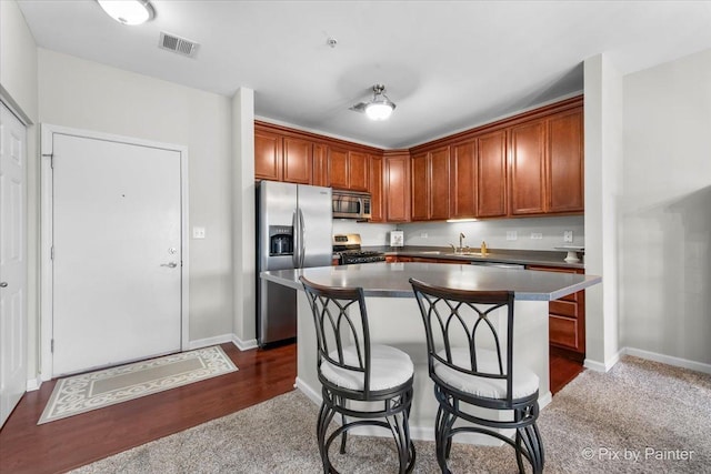 kitchen featuring visible vents, a kitchen island, a breakfast bar area, appliances with stainless steel finishes, and a sink