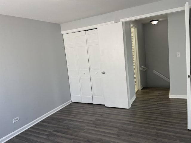 unfurnished bedroom featuring dark wood-style floors, baseboards, and a closet