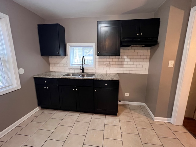 kitchen with under cabinet range hood, dark cabinets, tasteful backsplash, and a sink