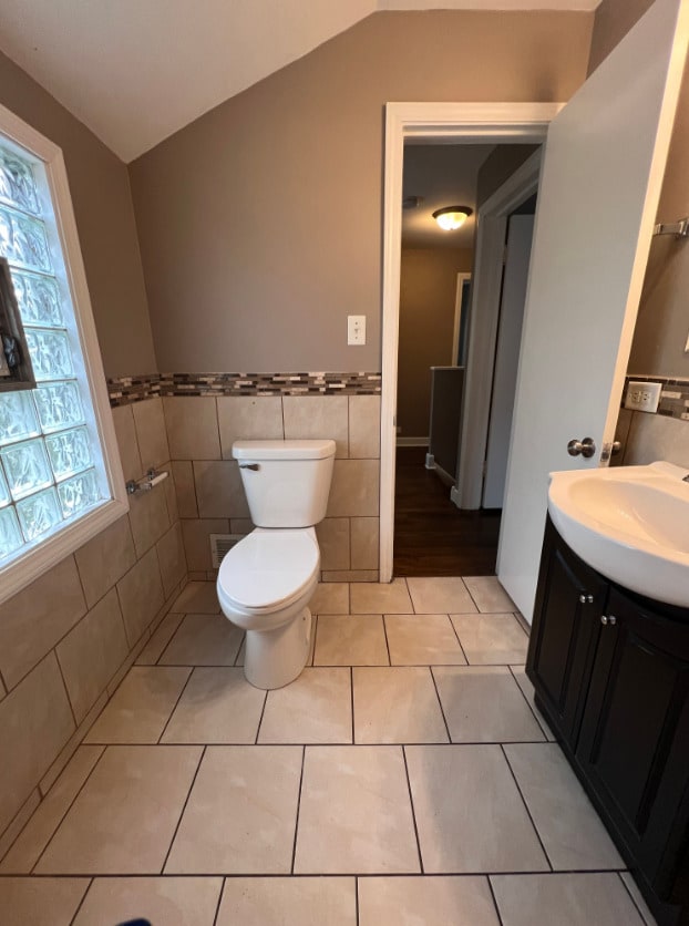 bathroom with vanity, lofted ceiling, tile walls, toilet, and tile patterned floors