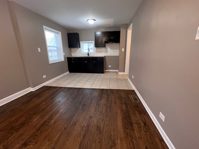 kitchen with baseboards, a sink, decorative backsplash, light countertops, and light wood-type flooring