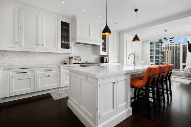 kitchen with a kitchen island with sink, backsplash, dark wood finished floors, white cabinetry, and glass insert cabinets