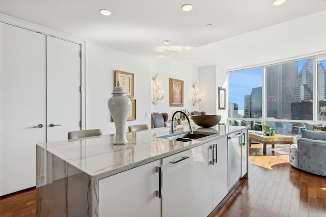 kitchen featuring dark wood finished floors, an island with sink, a sink, a city view, and open floor plan