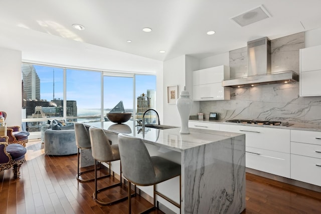 kitchen featuring modern cabinets, a sink, a kitchen breakfast bar, wall chimney range hood, and stainless steel gas cooktop