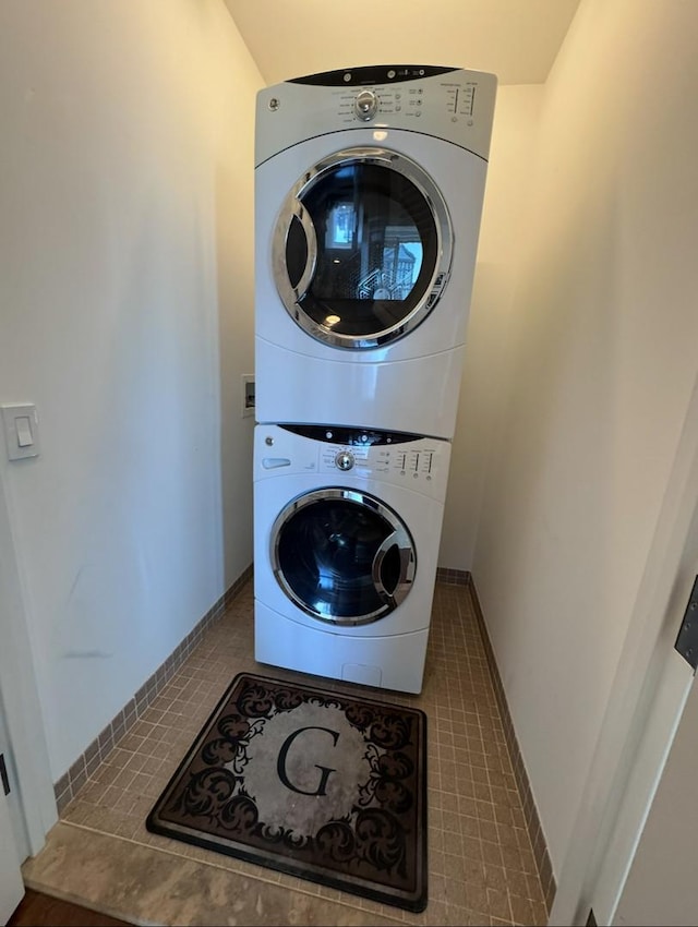 laundry room with tile patterned flooring, baseboards, and stacked washer / drying machine