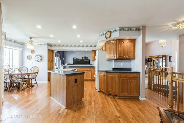 kitchen with dark countertops, light wood-type flooring, ceiling fan with notable chandelier, brown cabinetry, and a sink