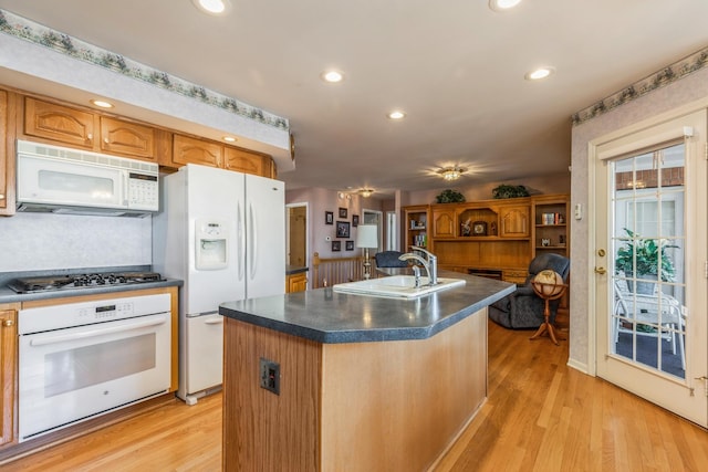 kitchen with a sink, light wood-style floors, white appliances, and dark countertops