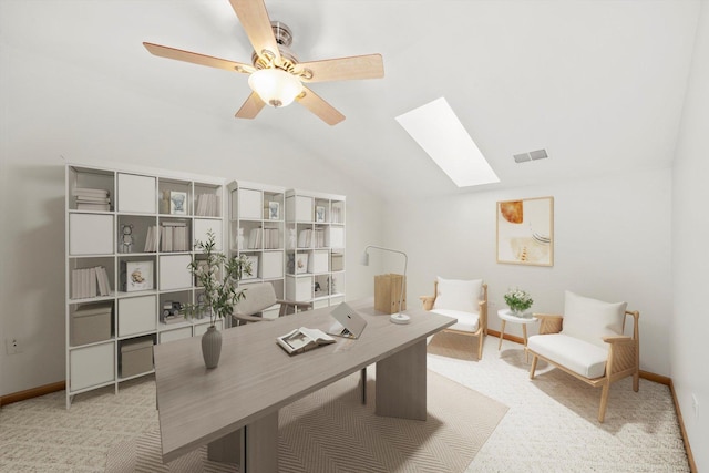 home office with visible vents, a ceiling fan, vaulted ceiling with skylight, carpet, and baseboards