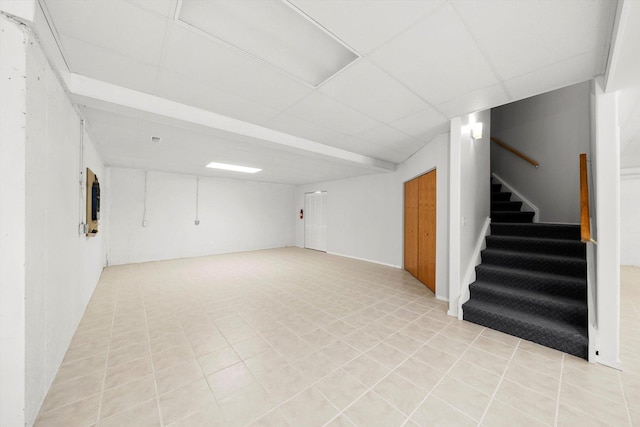 finished basement with light tile patterned flooring, stairway, and a paneled ceiling