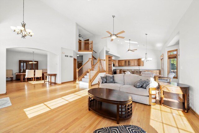 living area with light wood finished floors, ceiling fan with notable chandelier, arched walkways, and stairs