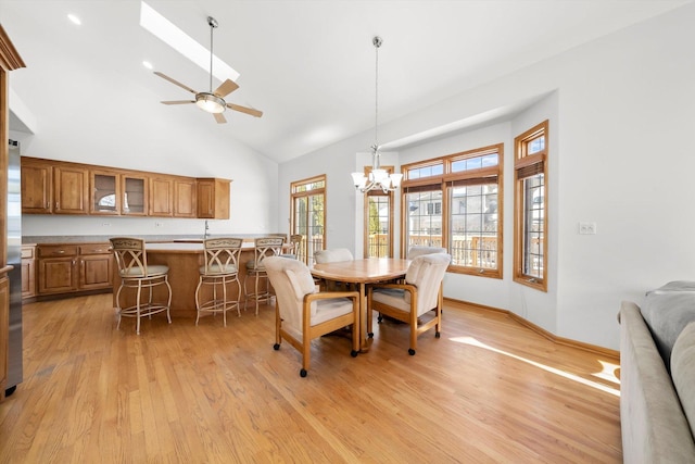 dining room with ceiling fan with notable chandelier, light wood-style flooring, high vaulted ceiling, and baseboards