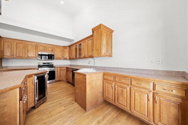 kitchen with a sink, stainless steel appliances, wine cooler, light wood-style floors, and light countertops