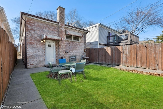 back of house with a lawn, brick siding, a fenced backyard, and a chimney