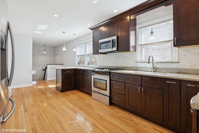 kitchen featuring a peninsula, light wood-style flooring, a sink, stainless steel appliances, and dark brown cabinets