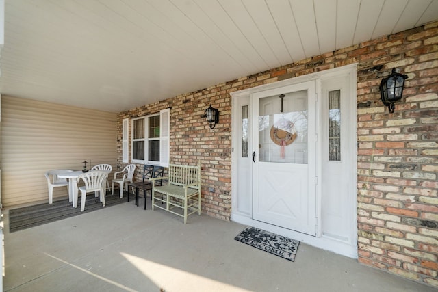 view of exterior entry featuring a porch and brick siding