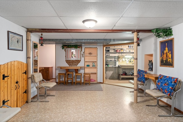 living area featuring tile patterned floors, a paneled ceiling, wood walls, and wainscoting