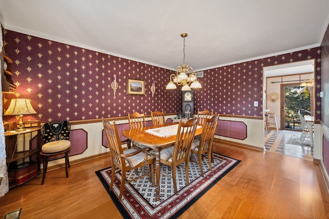 dining space with ornamental molding, wallpapered walls, an inviting chandelier, and wood finished floors