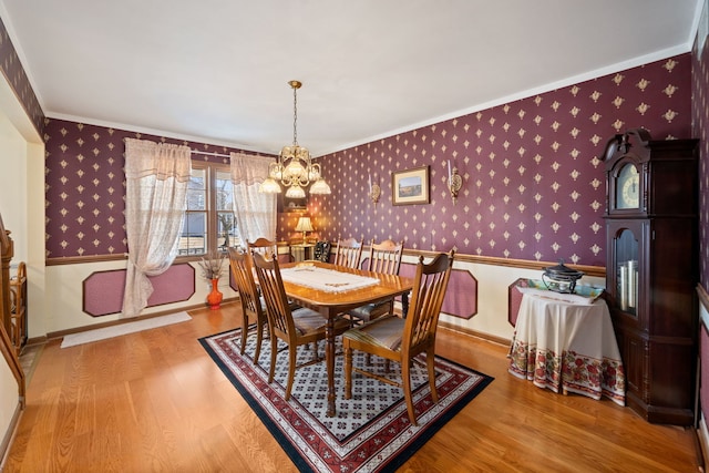 dining room featuring a notable chandelier, wood finished floors, crown molding, wallpapered walls, and baseboards