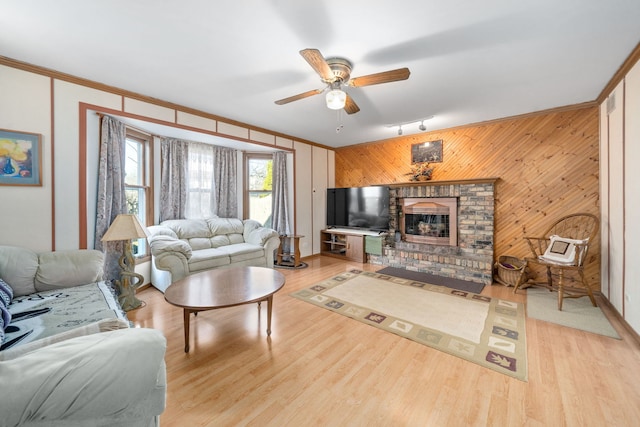 living area featuring light wood-style flooring, a fireplace, crown molding, and a ceiling fan