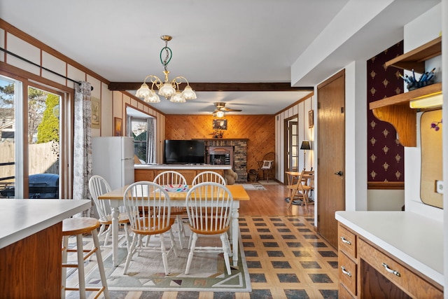 dining space with a fireplace, wood walls, dark floors, and ceiling fan with notable chandelier