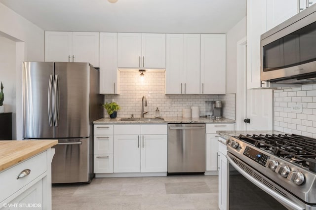 kitchen featuring backsplash, light stone counters, appliances with stainless steel finishes, white cabinets, and a sink