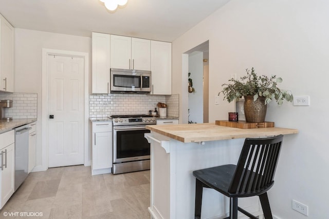 kitchen with a kitchen bar, tasteful backsplash, appliances with stainless steel finishes, white cabinets, and wooden counters