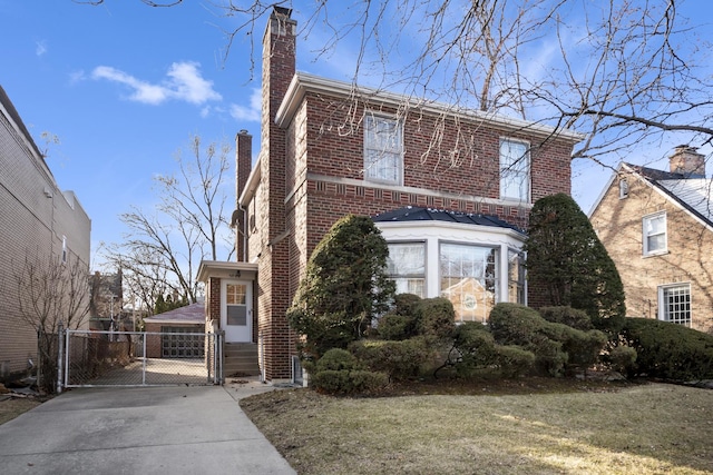 traditional-style home featuring a front yard, brick siding, a chimney, and a gate