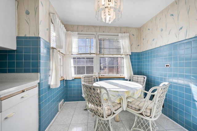 dining space with light tile patterned floors, wainscoting, wallpapered walls, and tile walls