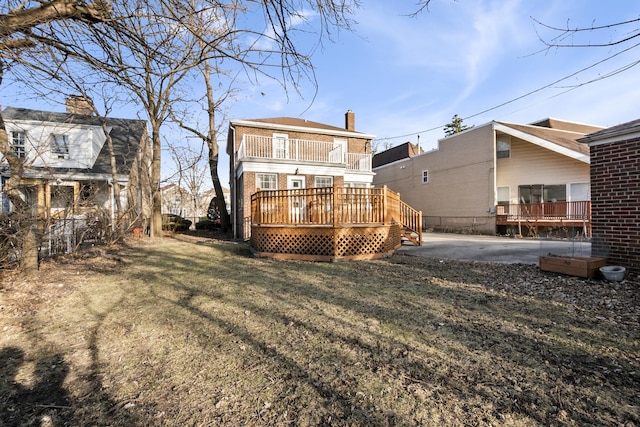 back of house with a deck, a balcony, a yard, brick siding, and a chimney