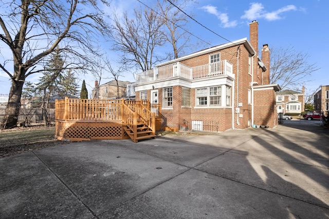 rear view of house with a balcony, brick siding, and a chimney