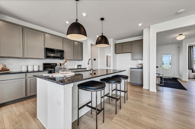 kitchen featuring black appliances, light wood-style flooring, a sink, backsplash, and dark stone counters