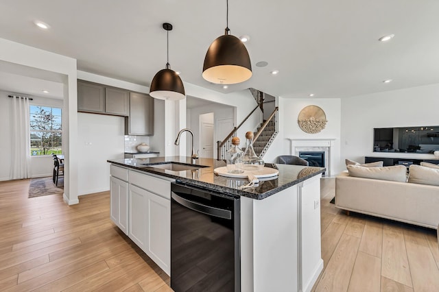 kitchen featuring open floor plan, black dishwasher, dark stone countertops, light wood-style flooring, and a sink