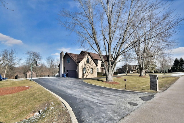 exterior space with a garage, driveway, a chimney, and a front lawn