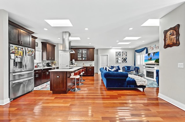 kitchen featuring island range hood, open floor plan, a skylight, and stainless steel refrigerator with ice dispenser