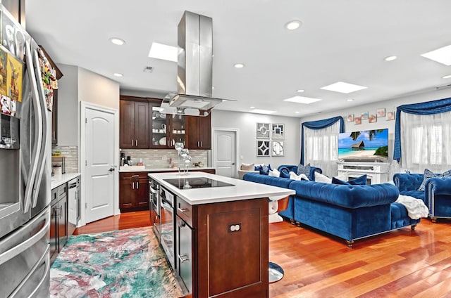 kitchen featuring island exhaust hood, freestanding refrigerator, light countertops, black electric stovetop, and open floor plan