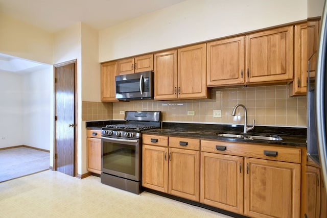 kitchen featuring a sink, backsplash, dark stone counters, appliances with stainless steel finishes, and brown cabinetry