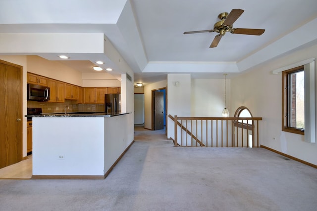 kitchen featuring a tray ceiling, appliances with stainless steel finishes, light carpet, dark countertops, and backsplash