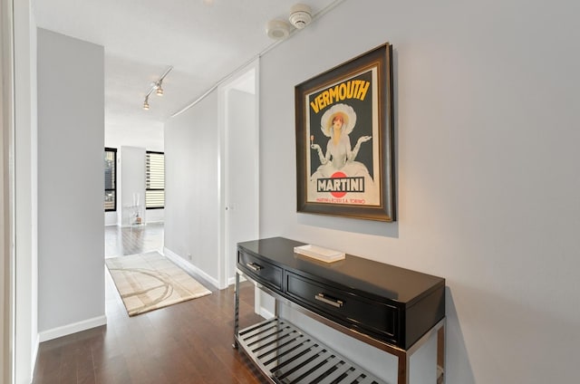 corridor featuring track lighting, dark wood-type flooring, and baseboards