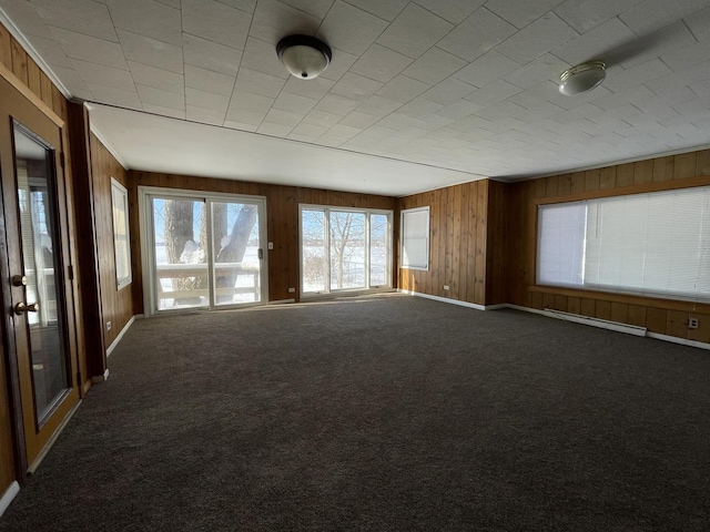 carpeted spare room featuring baseboards, baseboard heating, and wooden walls