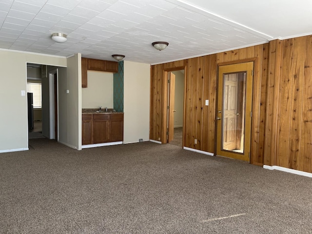 unfurnished room with crown molding, wooden walls, dark carpet, and a sink