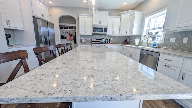 1617 Oliger Dr, Mahomet, IL 61853 - kitchen with light stone countertops, a spacious island, a sink, appliances with stainless steel finishes, and white cabinetry