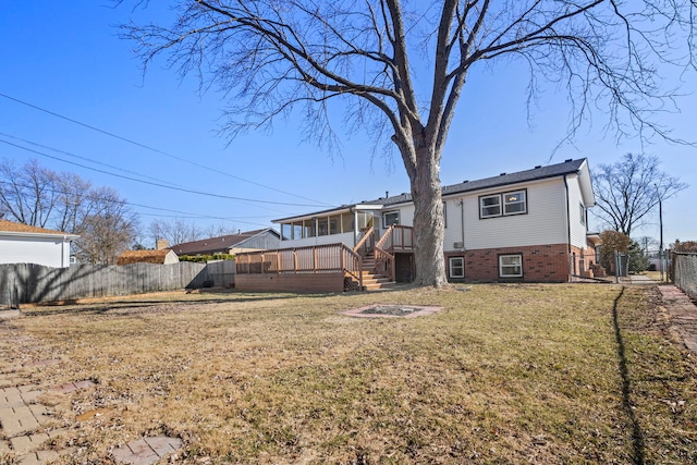 rear view of property featuring a fire pit, a wooden deck, a lawn, a fenced backyard, and a sunroom