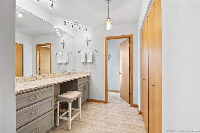 bathroom with baseboards, track lighting, wood finished floors, and vanity