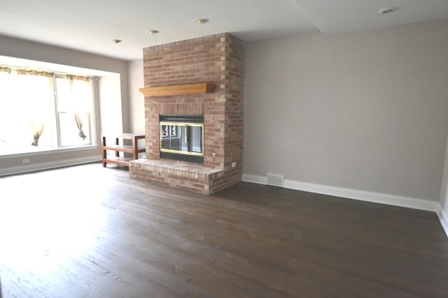 unfurnished living room featuring visible vents, a brick fireplace, baseboards, and wood finished floors