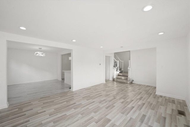 unfurnished living room featuring visible vents, baseboards, light wood-type flooring, stairs, and recessed lighting