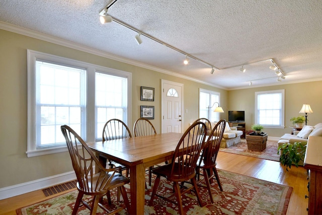 dining area featuring visible vents, a textured ceiling, crown molding, and wood finished floors