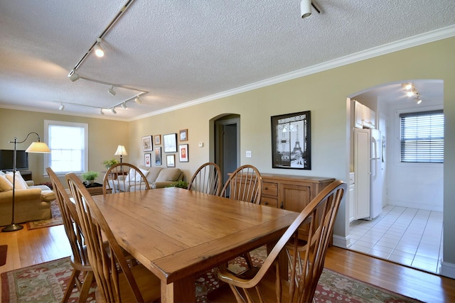 dining area with arched walkways, light wood-style floors, and ornamental molding