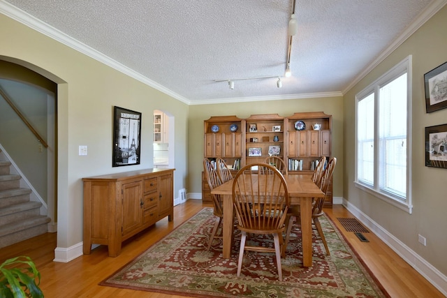 dining area featuring arched walkways, crown molding, a textured ceiling, and light wood-type flooring