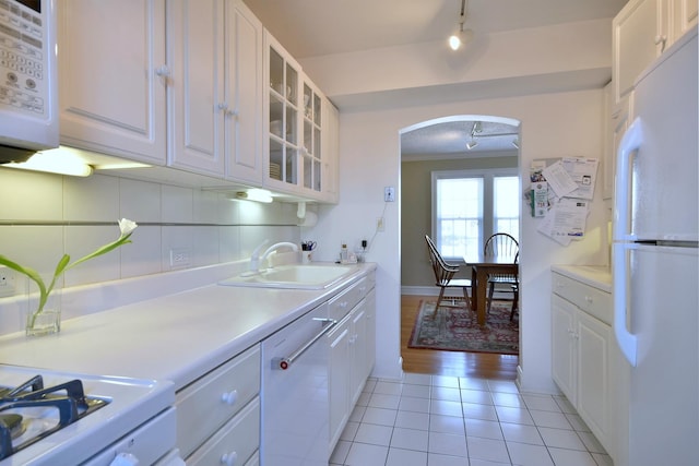 kitchen featuring white appliances, arched walkways, a sink, decorative backsplash, and white cabinetry