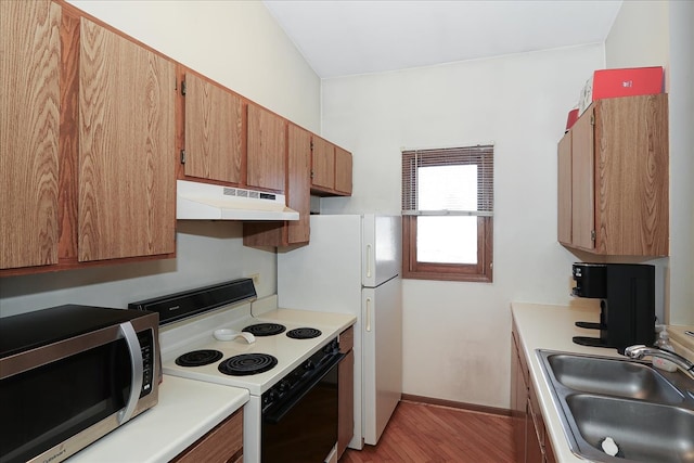 kitchen with a sink, range with electric cooktop, light countertops, under cabinet range hood, and stainless steel microwave